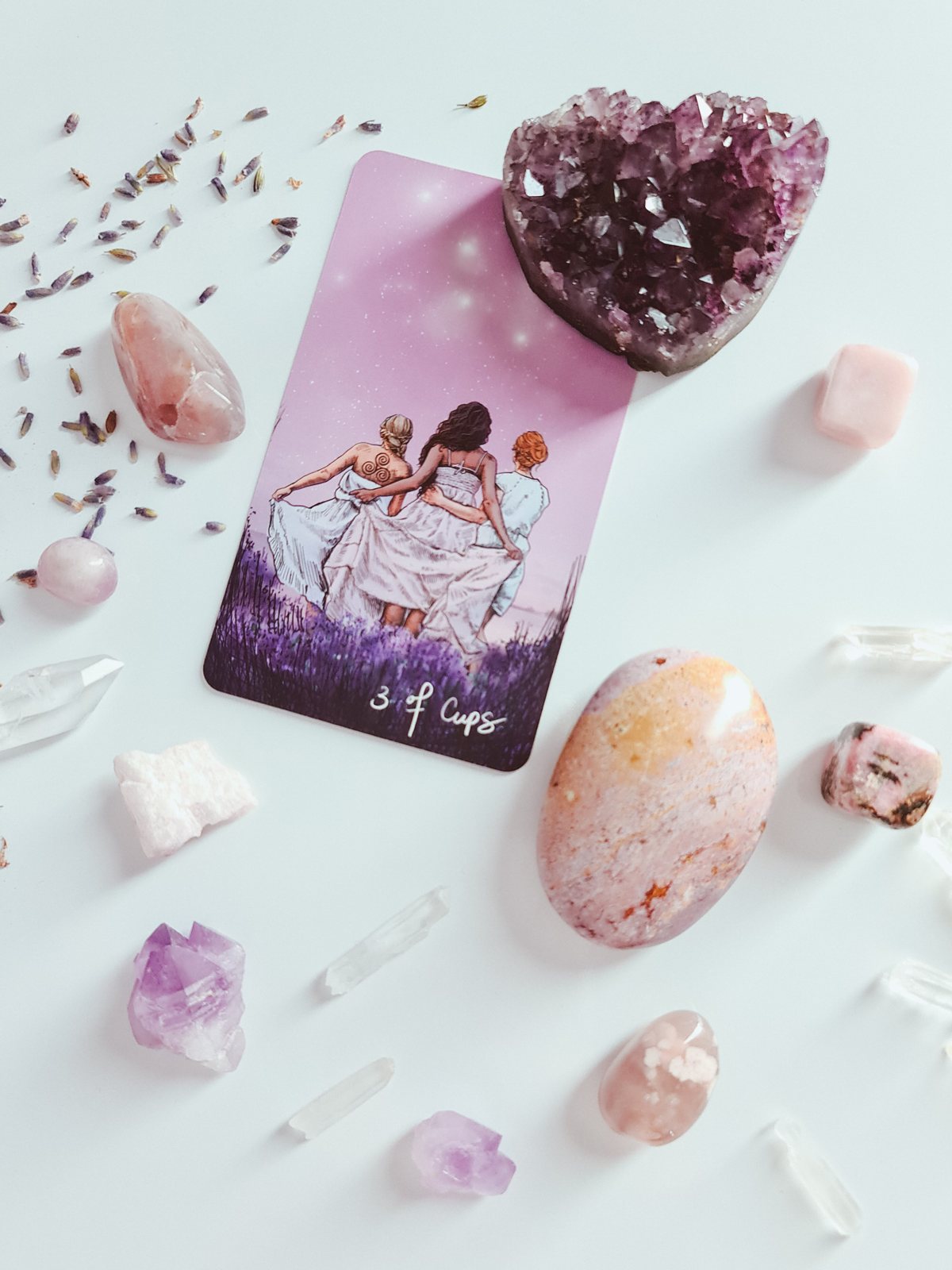 Une carte de tarot posée parmi des pierres roses et de la lavande